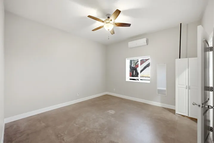 Apartment in the shop. Bedroom featuring light-colored walls, wood-finish ceiling fan, concrete flooring, and a window with horizontal blinds