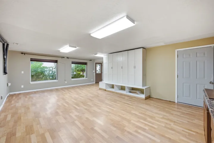 Main home basement. Spacious room with wood-finish flooring, multiple windows, and extensive built-in white cabinetry with integrated open shelving