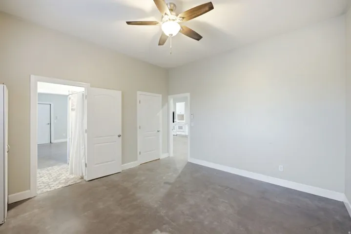 Apartment in the shop. Spacious room featuring light gray walls, a ceiling fan with wooden blades, and concrete flooring