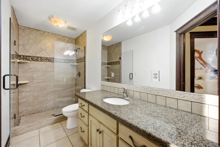 Main home upstairs. Full bathroom featuring a walk-in shower with glass enclosure, beige ceramic tile, and decorative accent banding