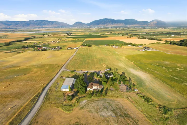 Expansive rural property featuring a main residence, additional structures, agricultural fields, and a distant mountain range backdrop