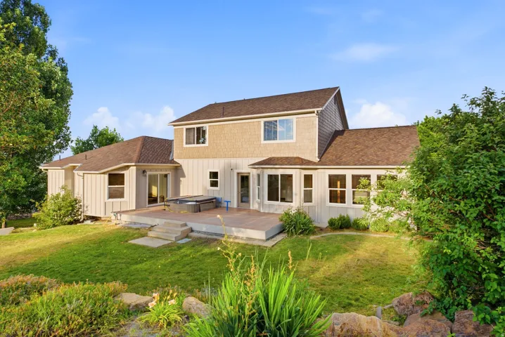 Rear exterior featuring a multi-level deck, board and batten siding, shake siding accents, multiple large windows, and a sloped lawn with mature landscaping