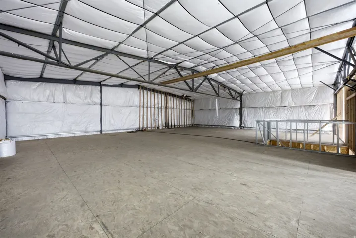 Expansive interior space featuring a concrete floor, exposed metal beam structure, and insulated walls and ceiling