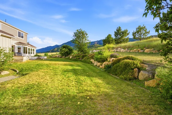 Spacious rear yard with a tiered landscape design featuring natural rock retaining walls, mature shrubs, and a sloped grassy area