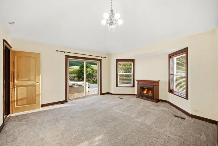 Master suite, Vaulted ceiling room with a decorative chandelier, dual windows with blinds, a corner fireplace, and sliding glass doors opening to a deck