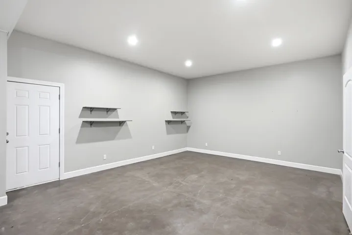 Apartment in the shop. Spacious room with concrete flooring, recessed lighting, white baseboards, and built-in wall shelving
