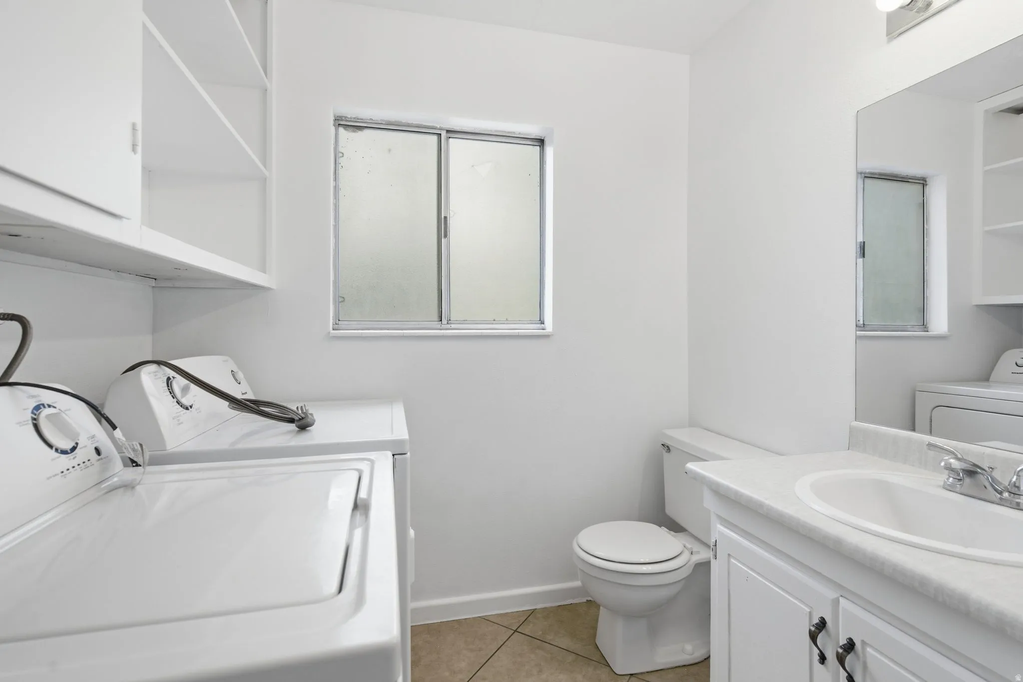 Utility room featuring a built-in shelf and cabinetry, a frosted window, a toilet, and a vanity with a white countertop and integrated sink