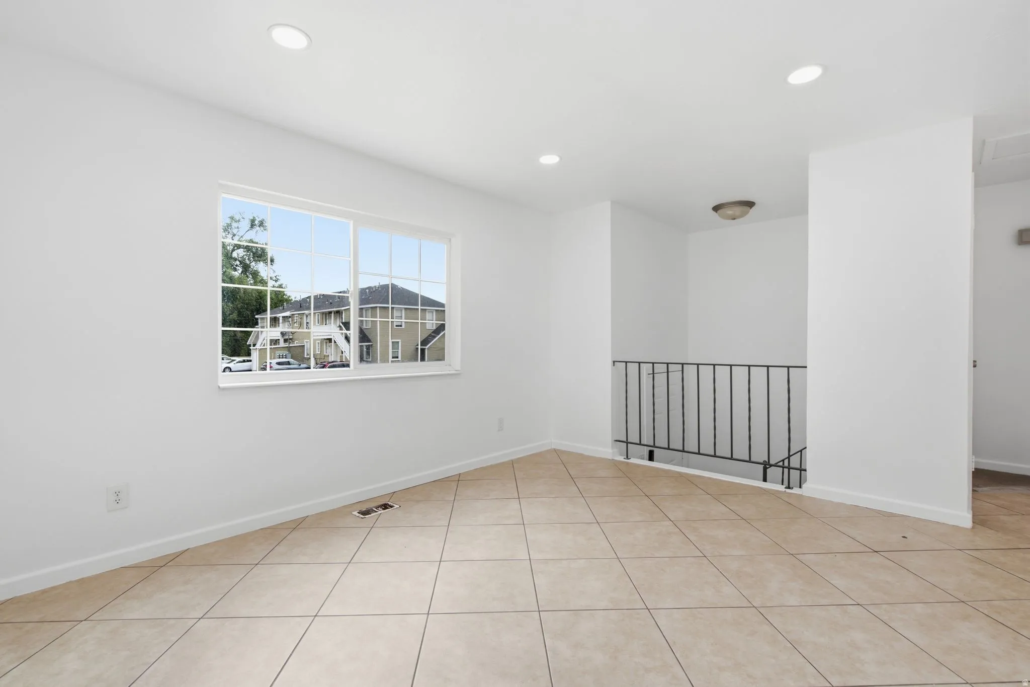 Spacious interior room featuring tile flooring, white walls, recessed ceiling lights, and a window providing natural light