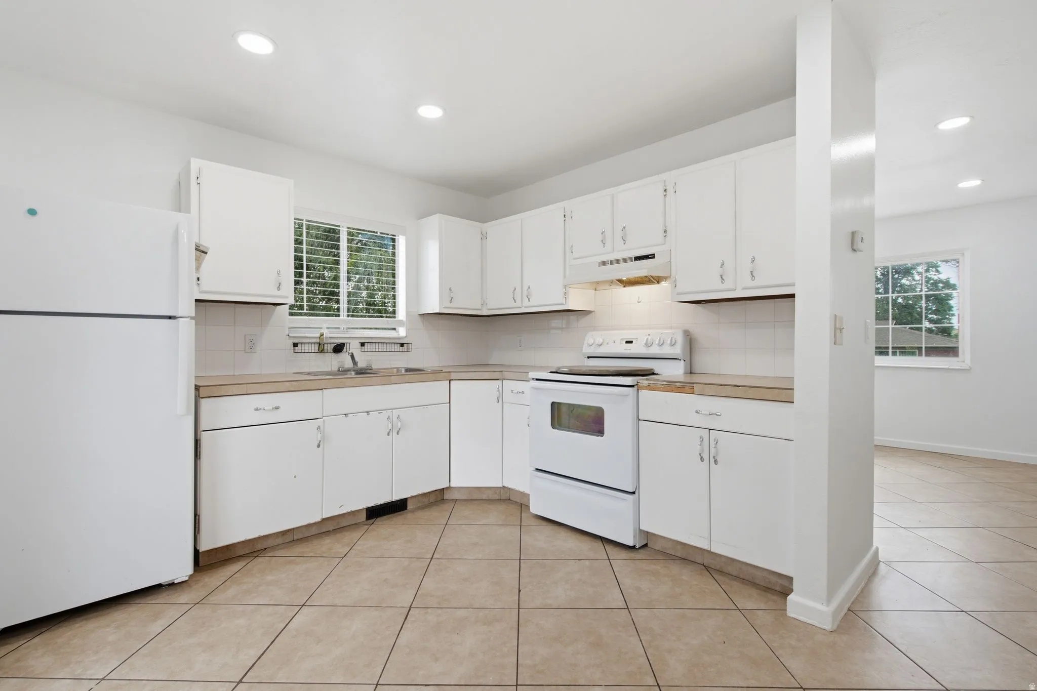 Bright kitchen featuring white cabinetry, a white refrigerator, a white electric range, recessed lighting, and tile flooring