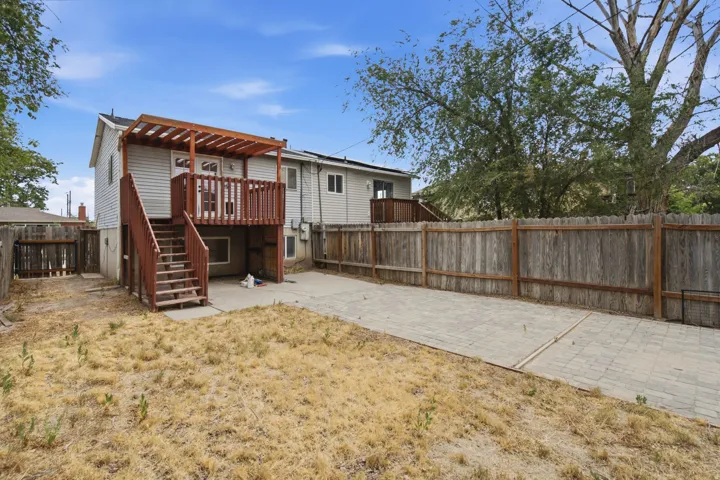 Rear exterior featuring a raised wooden deck with a pergola, exterior stairs, a privacy fence, and a paved patio area