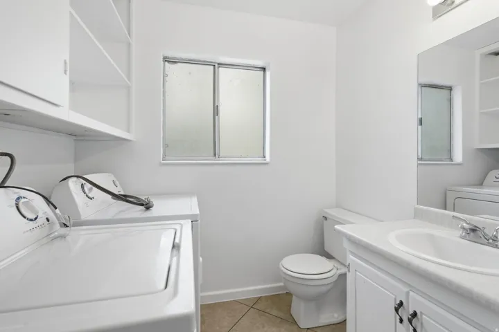 Utility room featuring a built-in shelf and cabinetry, a frosted window, a toilet, and a vanity with a white countertop and integrated sink