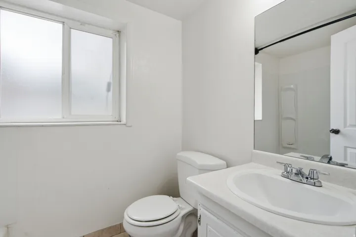 Bathroom featuring a frosted window, white vanity with integrated sink, chrome faucet, wall-mounted mirror, and a white commode