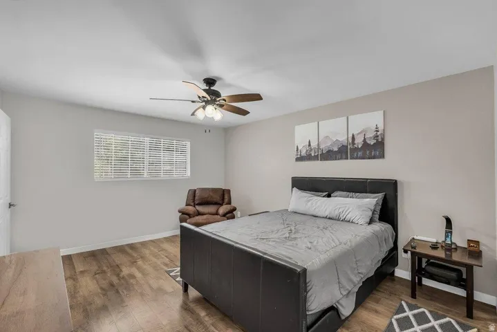 Spacious room featuring wood-finish flooring, a ceiling fan with integrated lighting, and a window with horizontal blinds
