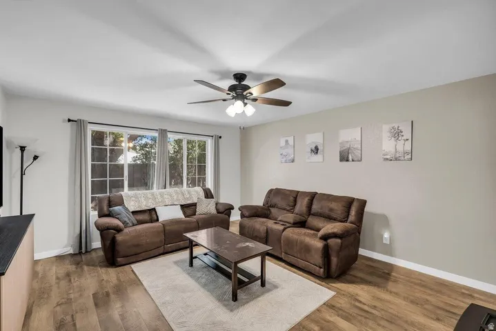 Living area featuring wood-finish flooring, a contemporary ceiling fan with integrated lighting, and multiple large windows