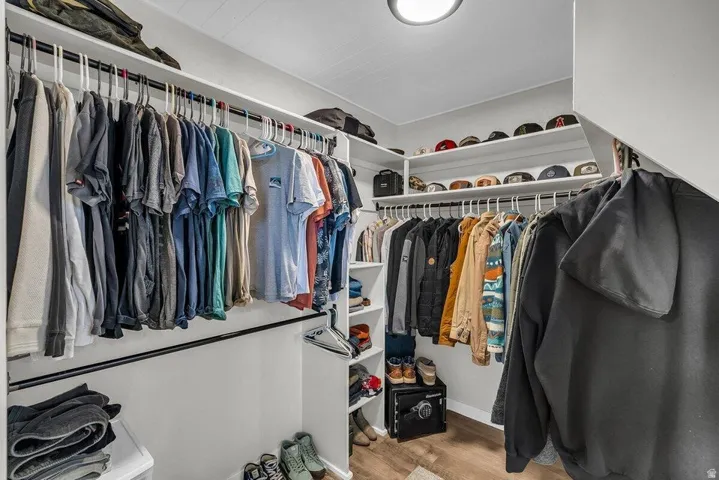 Walk-in closet featuring built-in shelving, multiple hanging rods, wood-finish flooring, and a flush-mount ceiling light