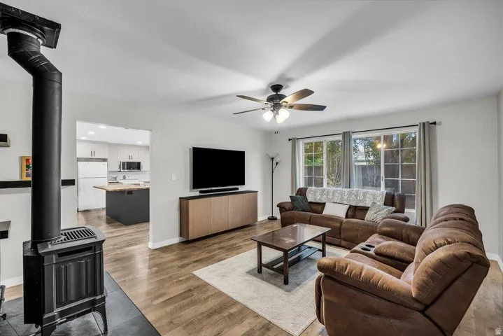 Living area featuring a freestanding wood-burning stove, wood-finish flooring, and a ceiling fan with integrated lighting
