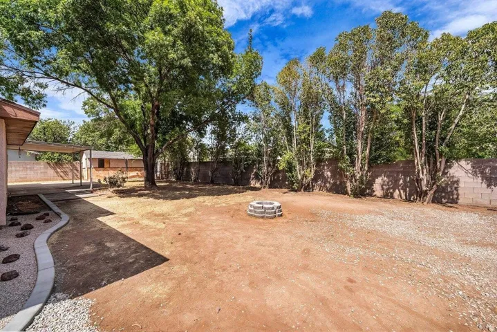 Expansive backyard featuring a large mature tree, a covered patio area, a block wall perimeter, and a central circular fire pit