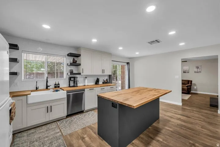 Kitchen featuring a central island with a wood-finish countertop, white cabinetry with black hardware, a farmhouse sink, stainless steel appliances, and wood-finish flooring