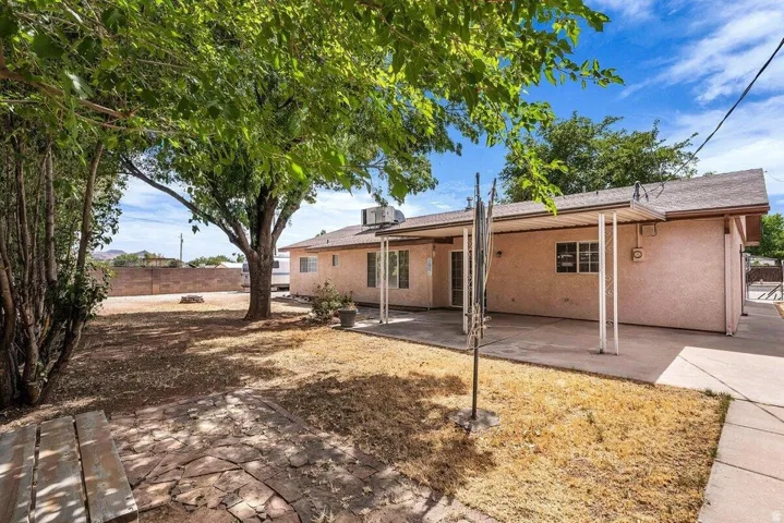Spacious backyard featuring a large mature tree providing shade, a concrete patio, a flagstone patio area, and a stucco exterior