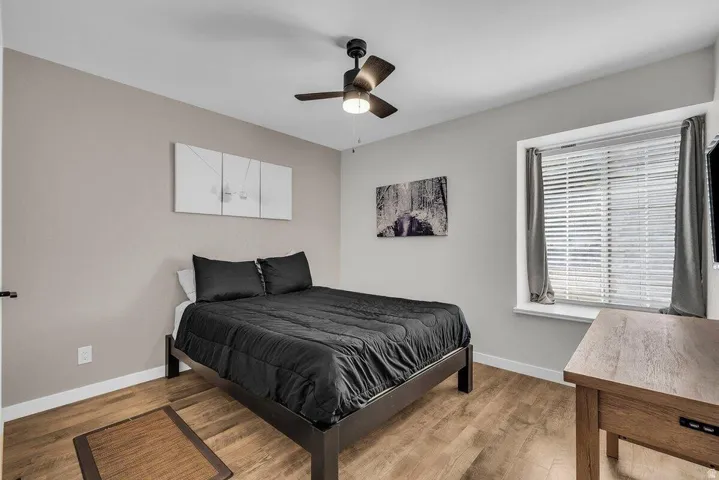 Bedroom featuring wood-finish flooring, a ceiling fan with integrated lighting, a window with horizontal blinds, and neutral-toned walls