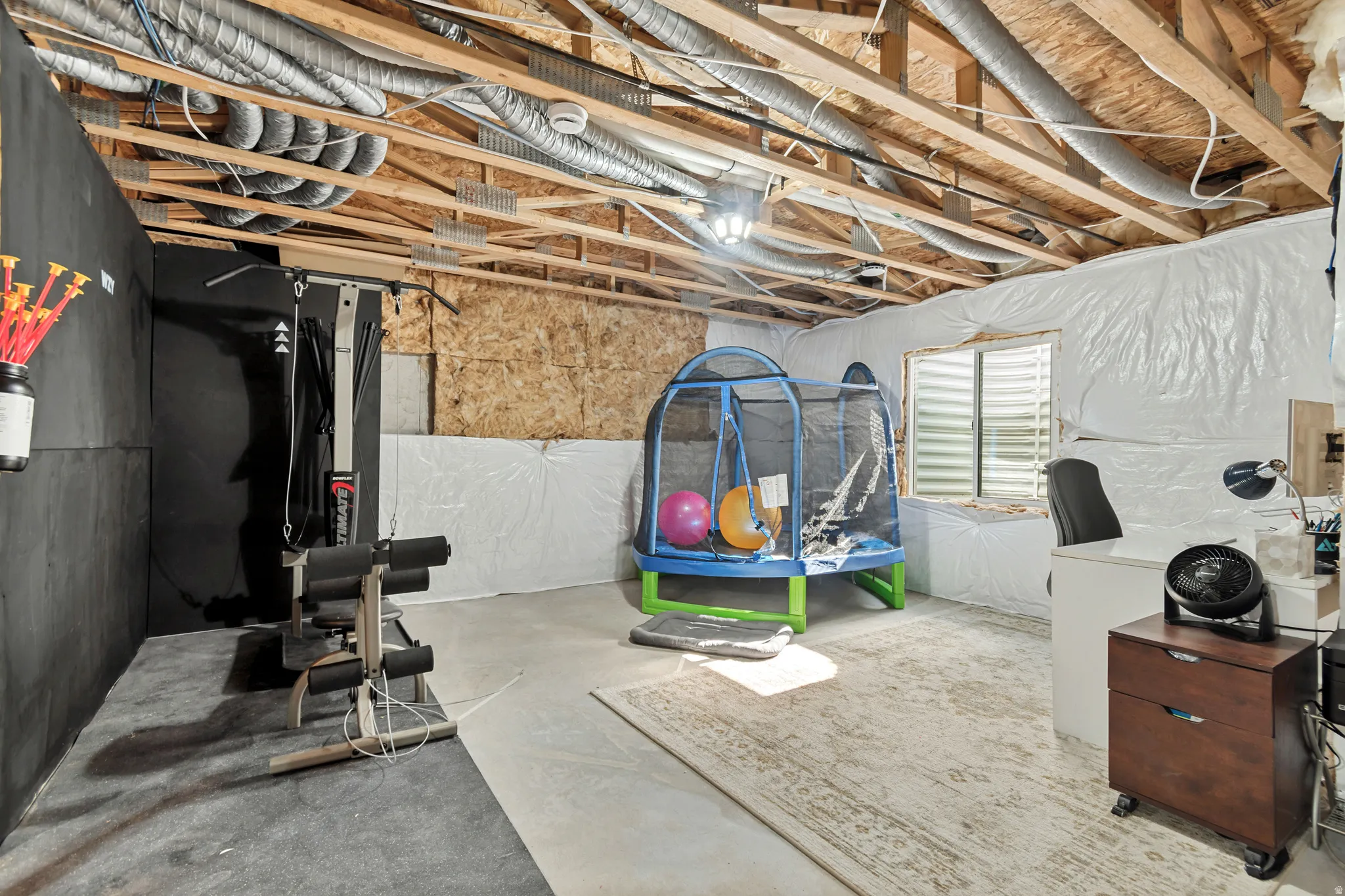 Unfinished basement featuring exposed ceiling joists and ductwork, concrete flooring, and a large window