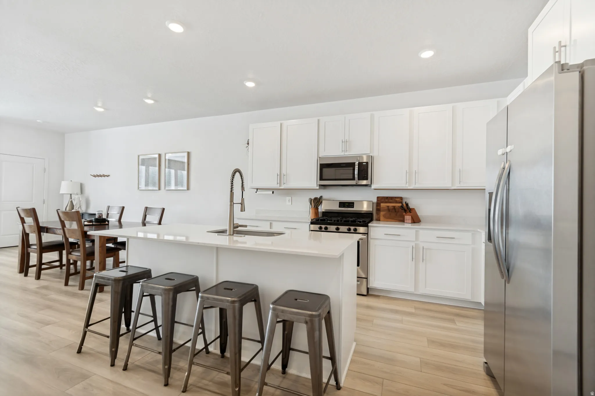 Modern kitchen featuring a central island with integrated sink, stainless steel appliances, white cabinetry, and light wood-finish flooring