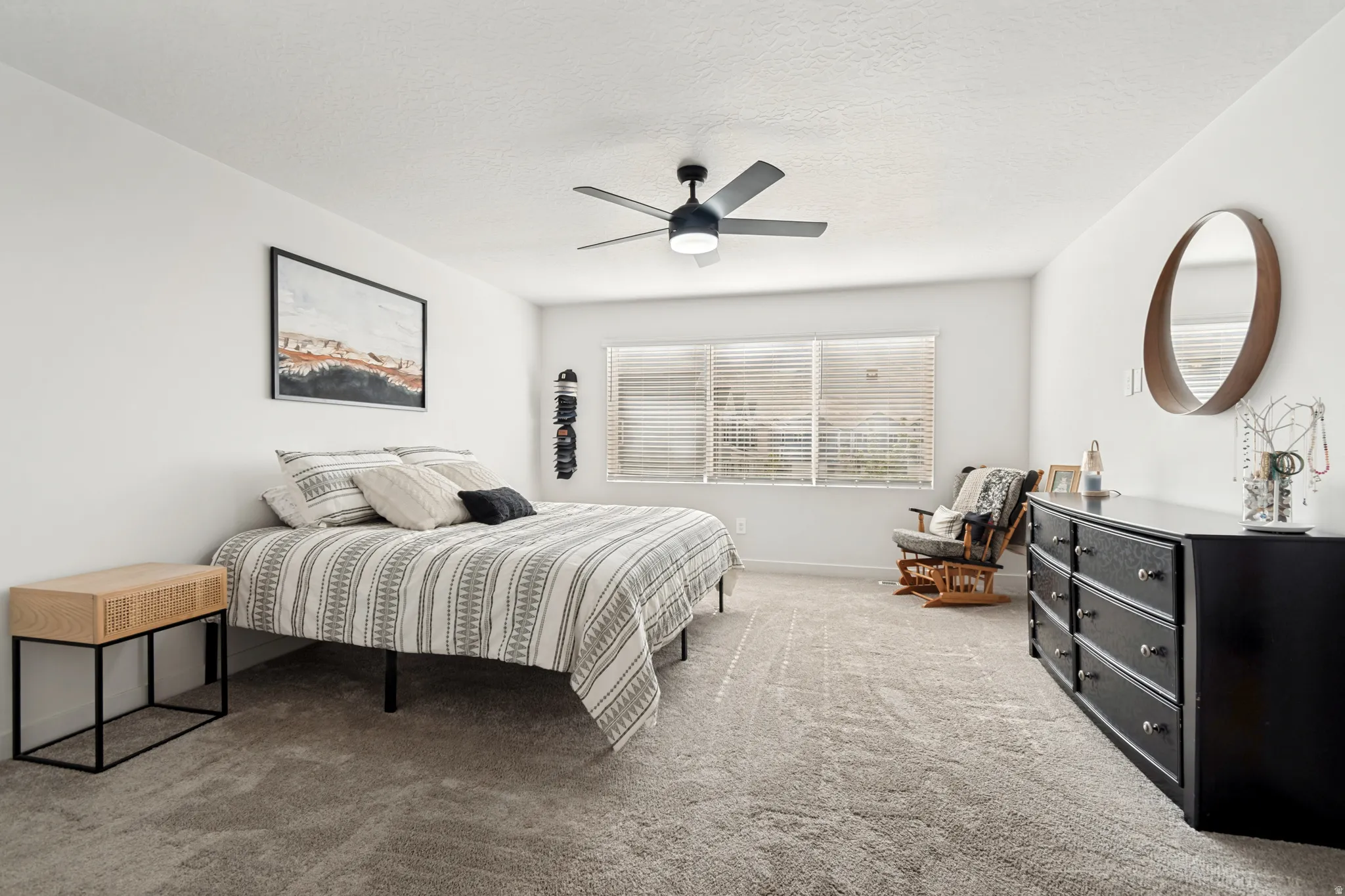 Spacious room featuring light gray carpeting, neutral wall finishes, a multi-pane window with blinds, and a ceiling fan with integrated lighting