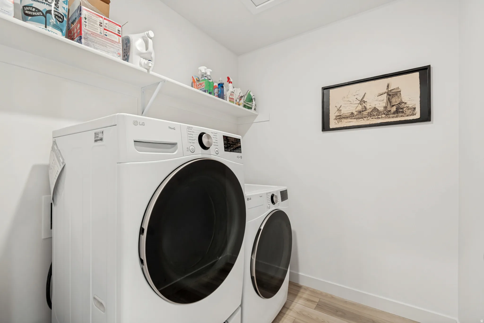 Dedicated laundry area featuring modern white appliances, light wood-finish flooring, and wall-mounted shelving for storage