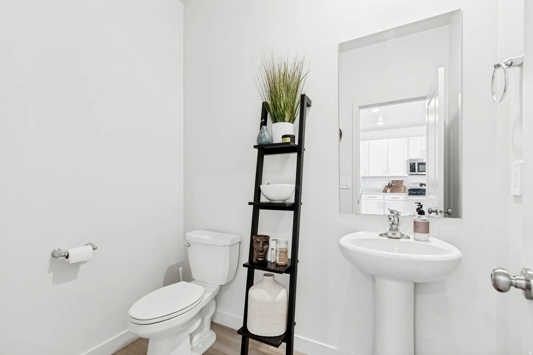 Pedestal sink with chrome faucet, wall-mounted mirror, and wood-finish flooring