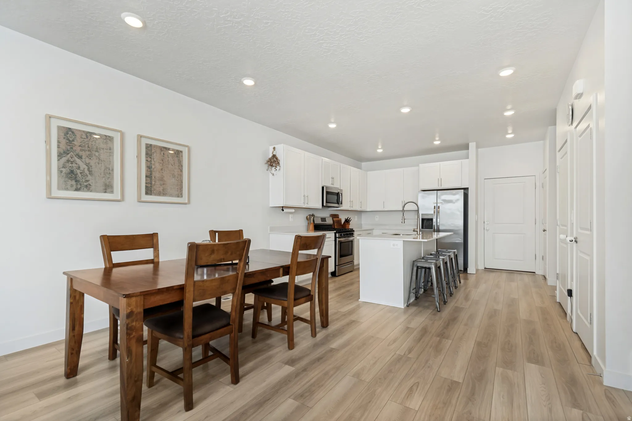 Open-concept living space featuring wood-finish flooring, recessed lighting, and a kitchen with white cabinetry and stainless steel appliances