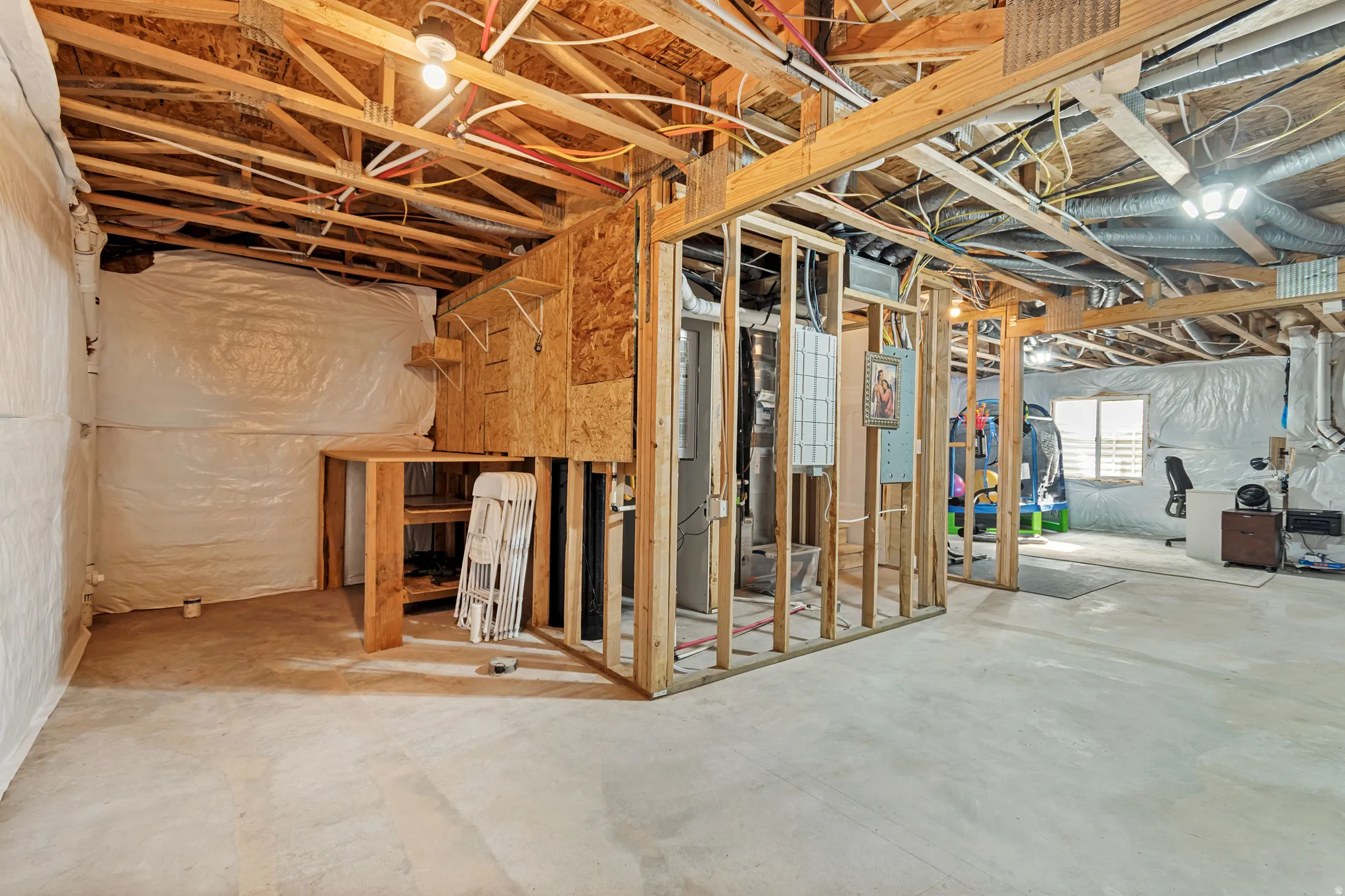 Unfinished basement space with exposed wooden joists and framing, concrete flooring, and a large window providing natural light
