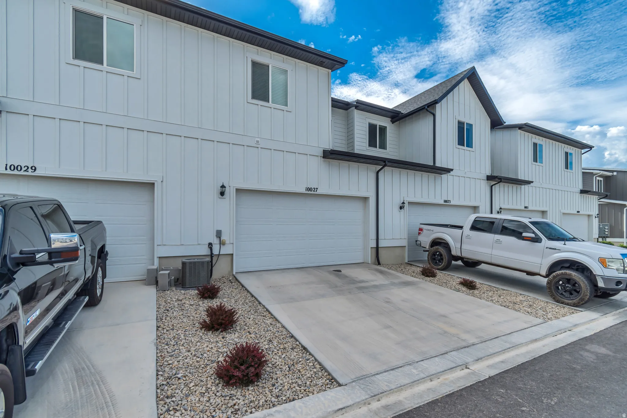Contemporary townhome exterior featuring white board and batten siding, dark trim accents, and attached garages