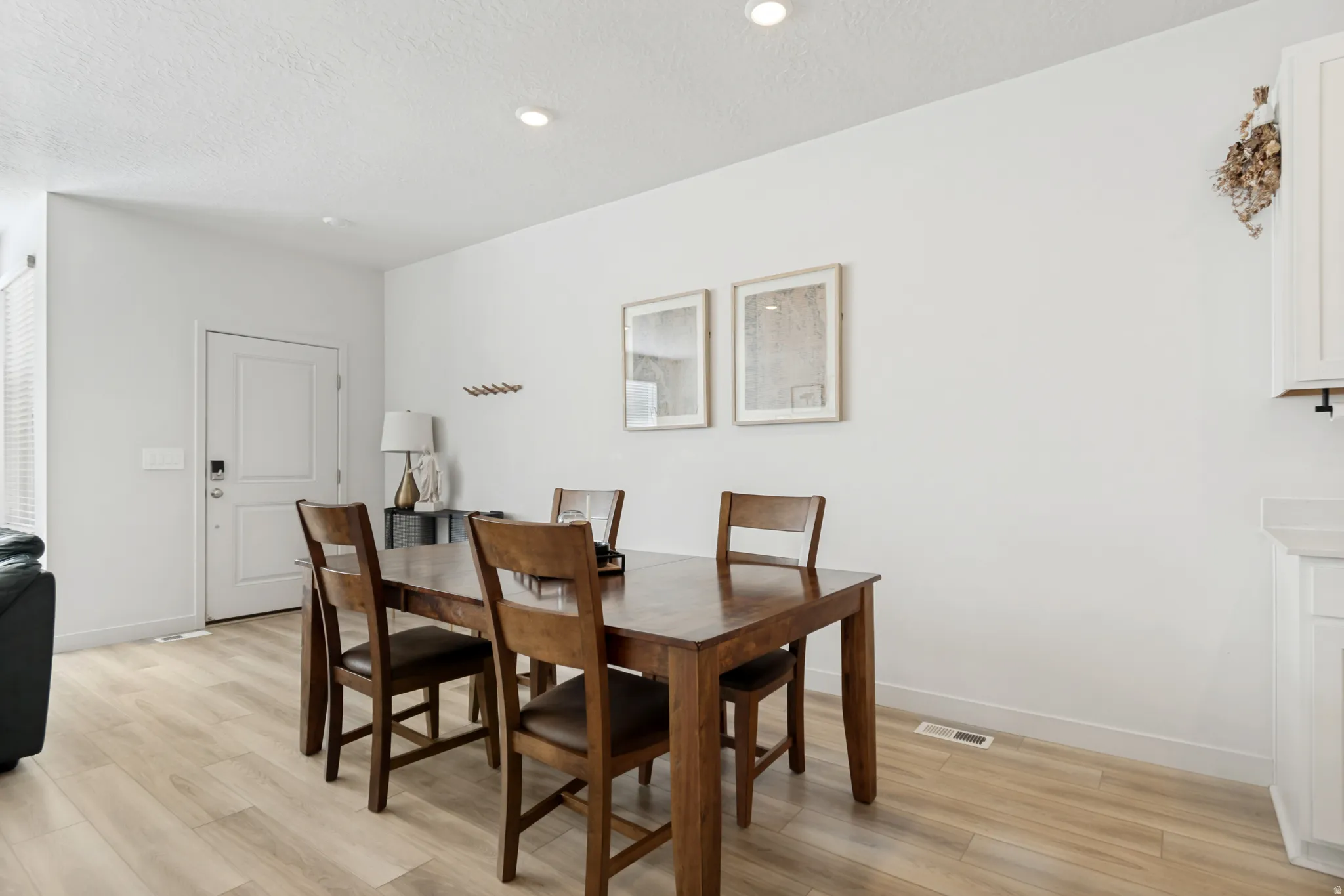 Open-concept dining area featuring light wood-finish flooring, recessed lighting, and a white entry door with smart lock hardware