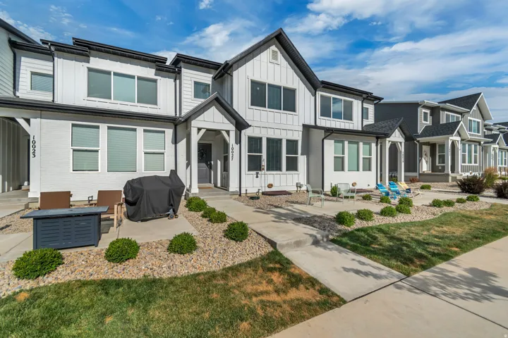 Modern townhouse exterior featuring white siding, dark trim, a covered entry, and a concrete patio