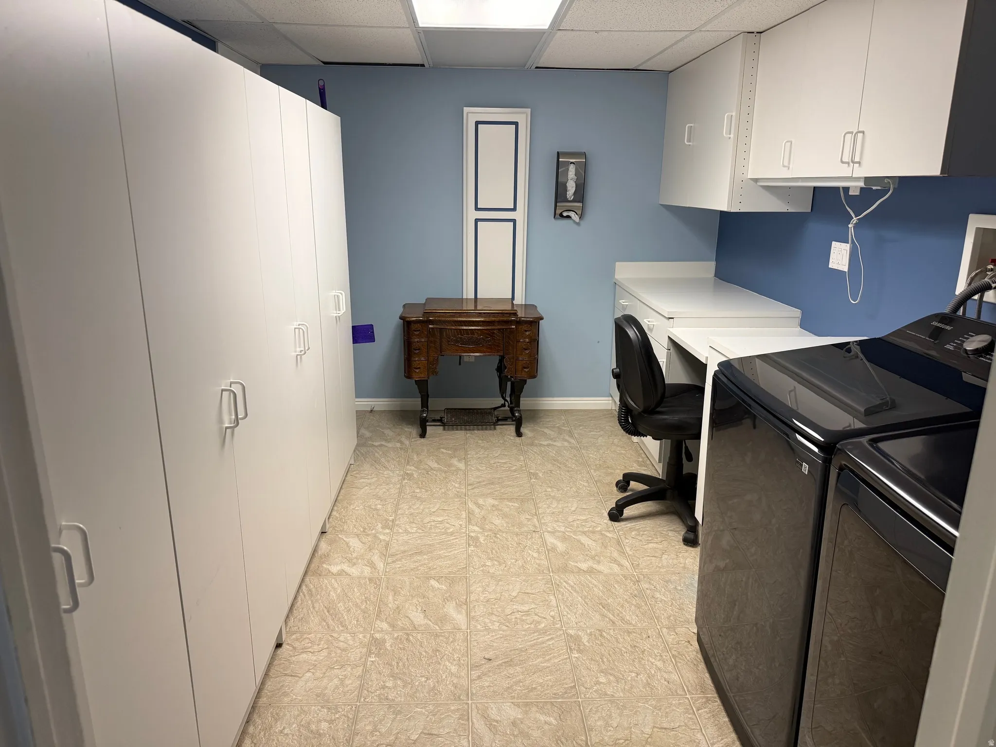 Utility room featuring extensive white built-in cabinetry, light-toned flooring, and a blue accent wall