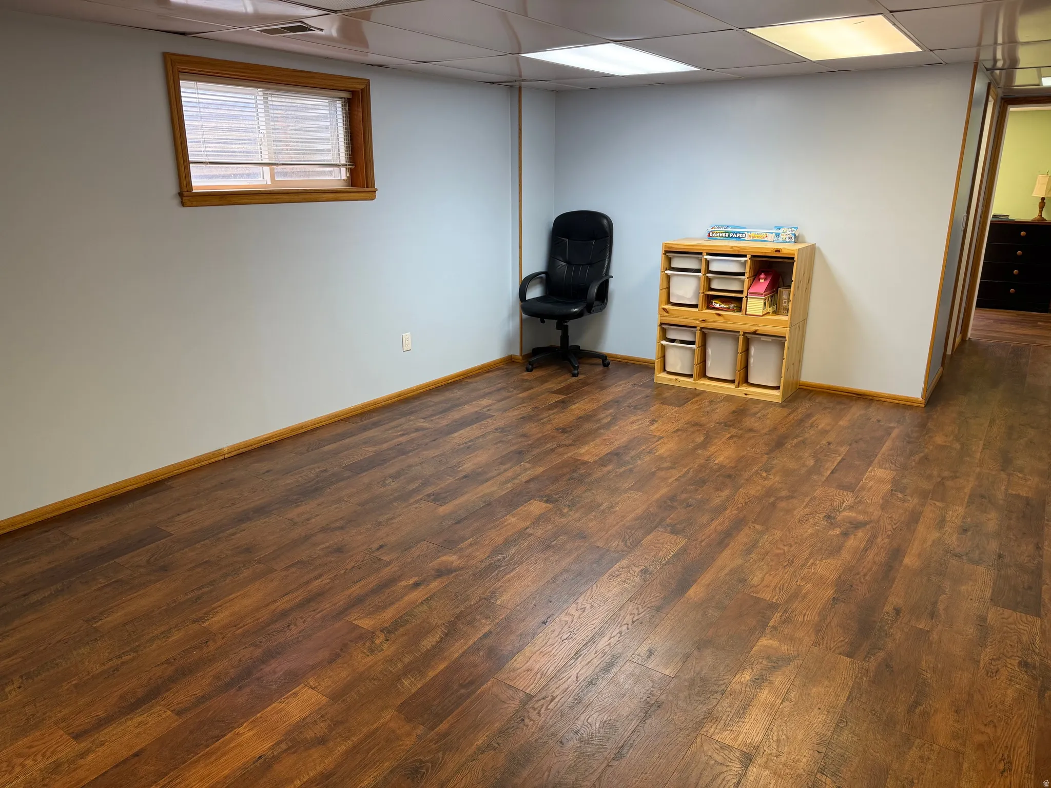 Spacious room featuring wood-finish flooring, a window with natural wood trim, and light blue walls