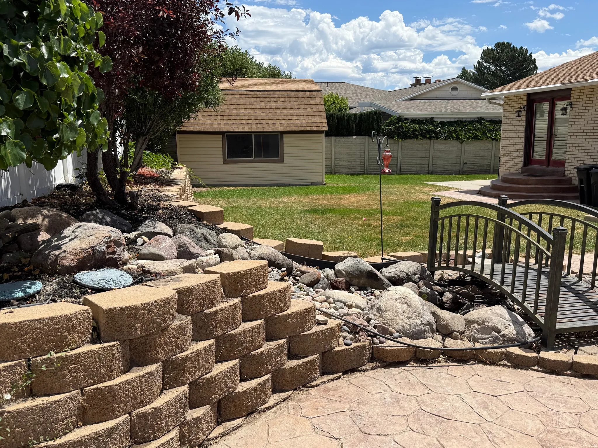 Backyard oasis featuring a stamped concrete patio, stone retaining wall, decorative rock features, and a small ornamental bridge