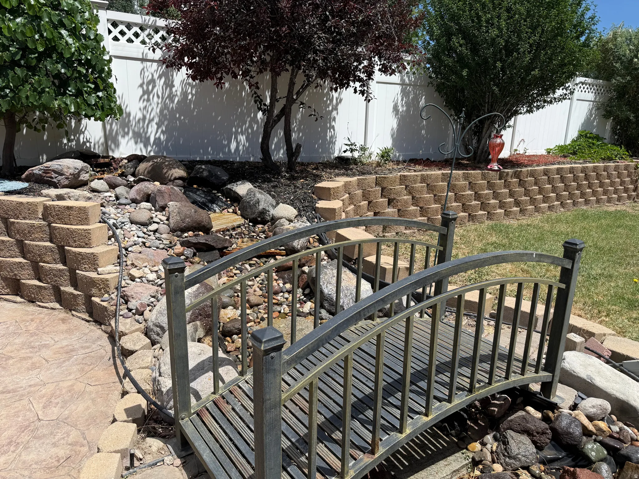 Decorative metal footbridge crossing a rock-lined water feature with tiered retaining walls