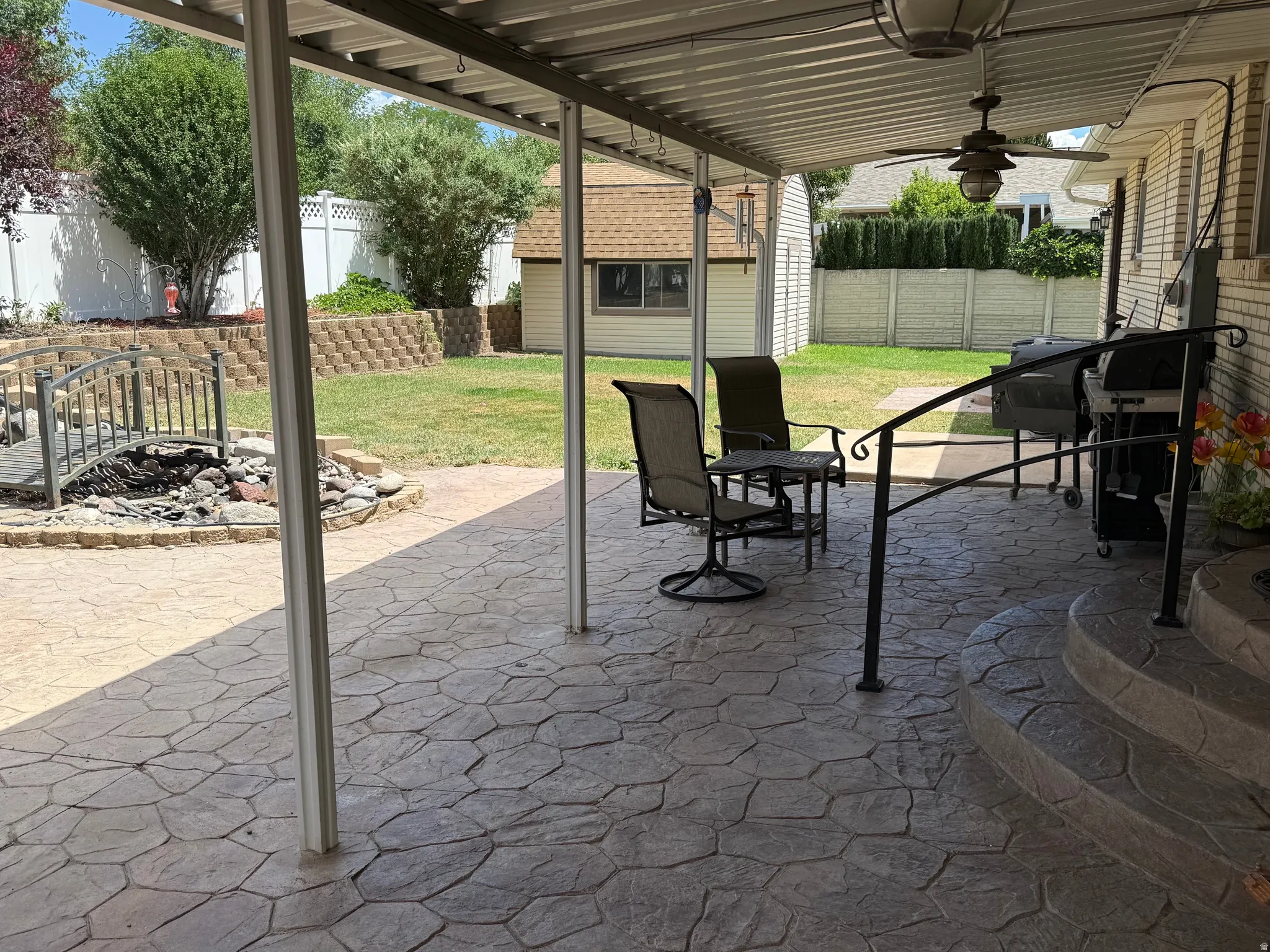 Covered patio featuring stamped concrete flooring, a ceiling fan with integrated lighting, and a black wrought iron railing