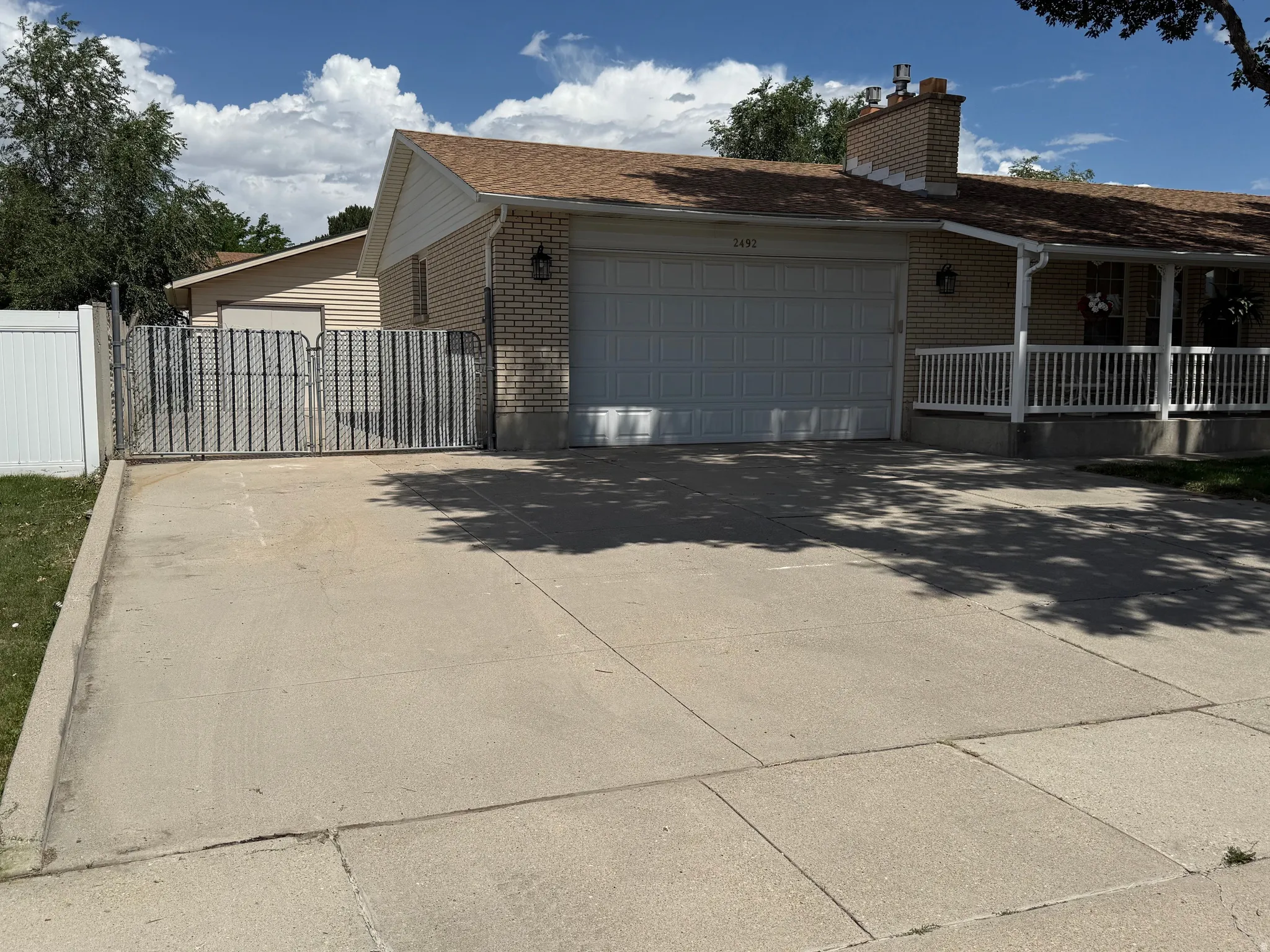 Large RV parking behind the gate. Front exterior featuring a two-car garage, concrete driveway, and covered porch with white railings