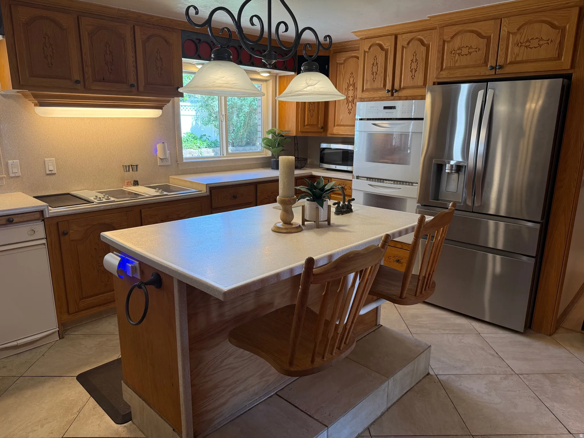 Kitchen featuring wood cabinetry, a center island with countertop seating, stainless steel refrigerator, double wall oven, and tile flooring