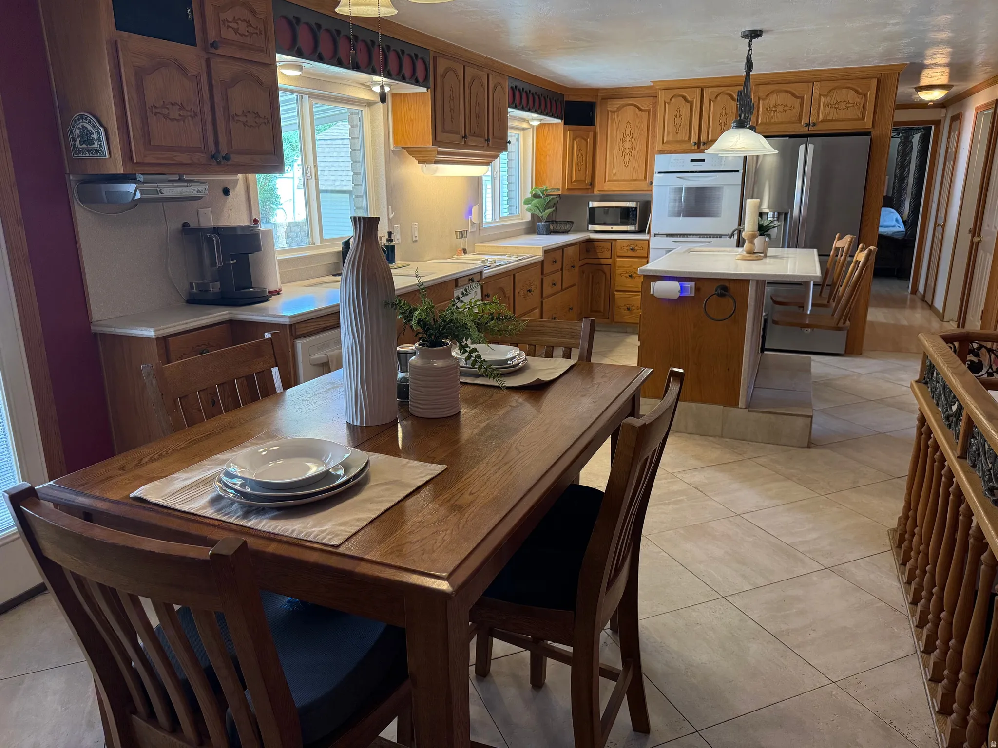 Kitchen and dining area featuring warm-toned custom wood cabinetry, built-in oven, stainless steel refrigerator, and light-toned tile flooring