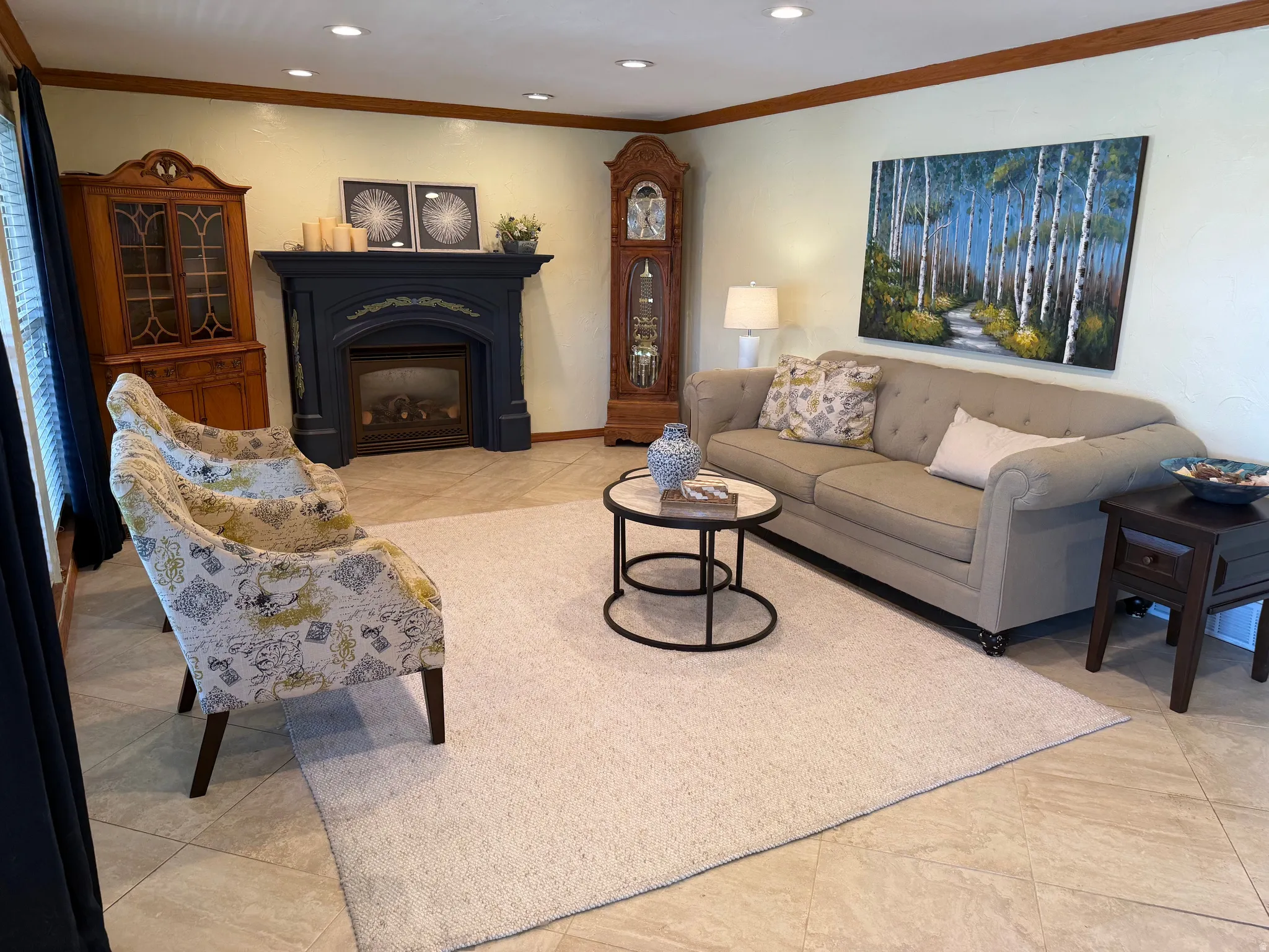 Spacious living area featuring light-toned tile flooring, recessed lighting, and a prominent fireplace with an ornate dark mantel