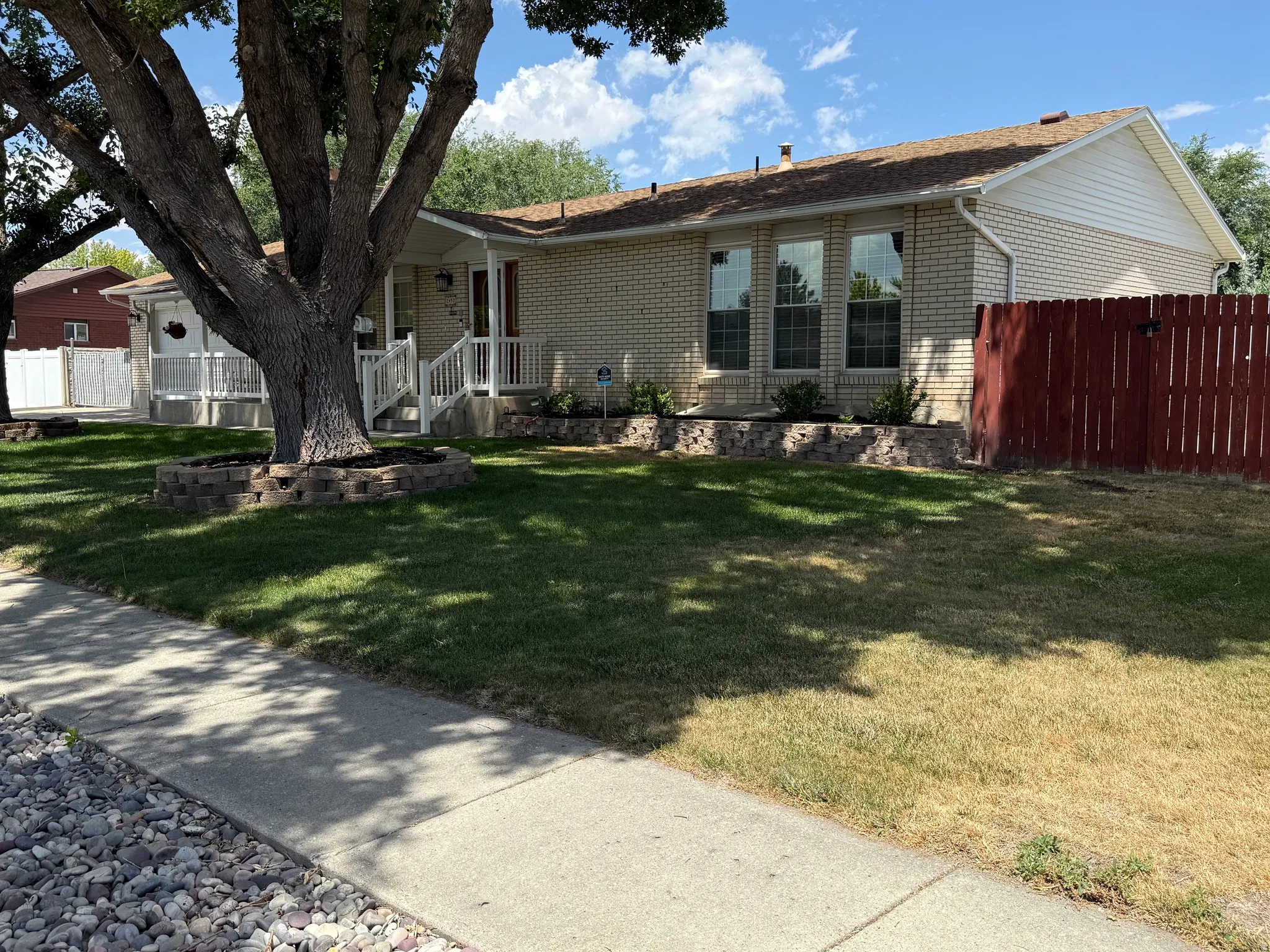 2 Large mature trees. Brick exterior home with a brown shingle roof and a red painted privacy fence