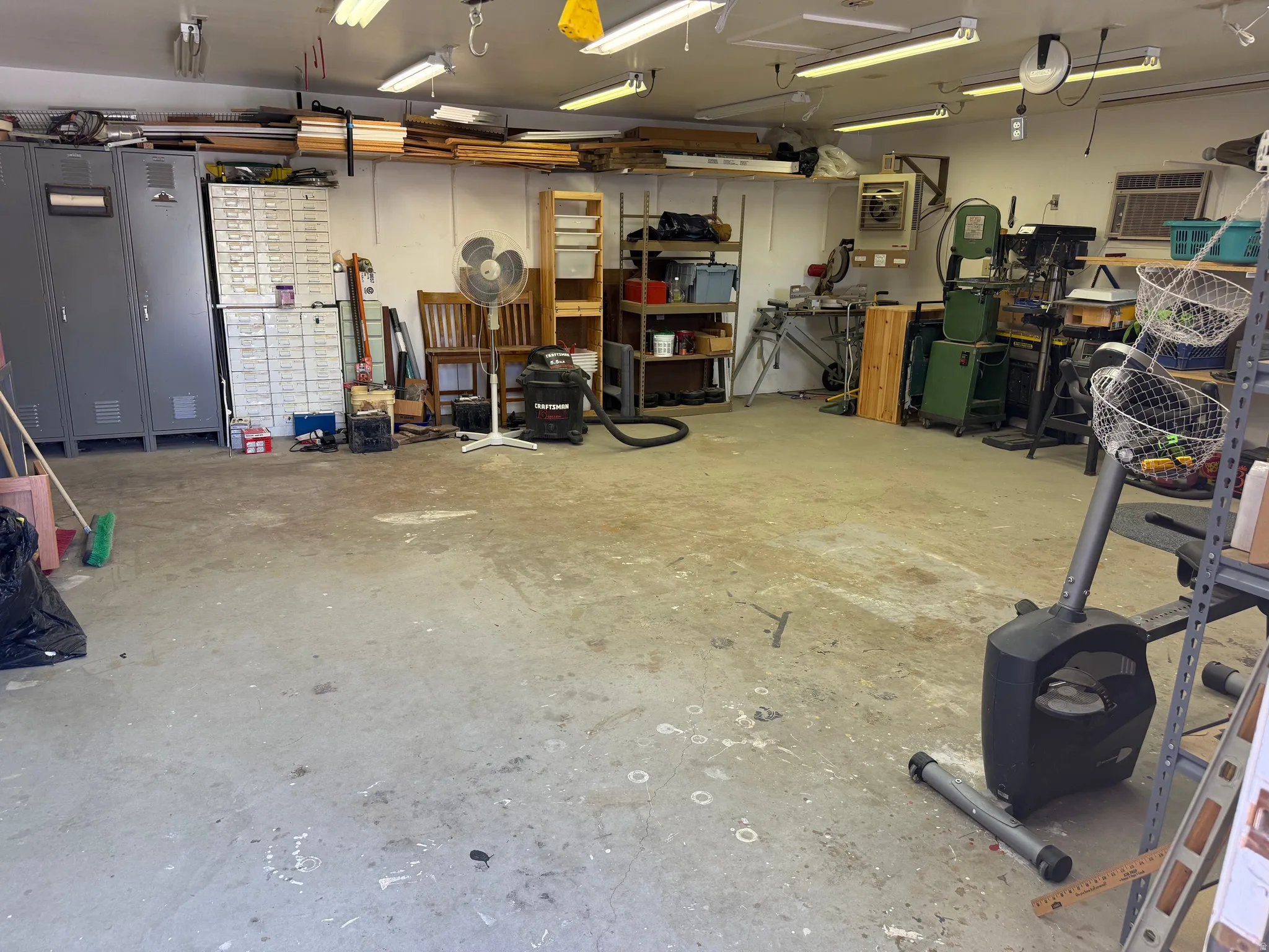 Spacious garage featuring concrete flooring, overhead fluorescent lighting, wall-mounted shelving, and built-in storage cabinets