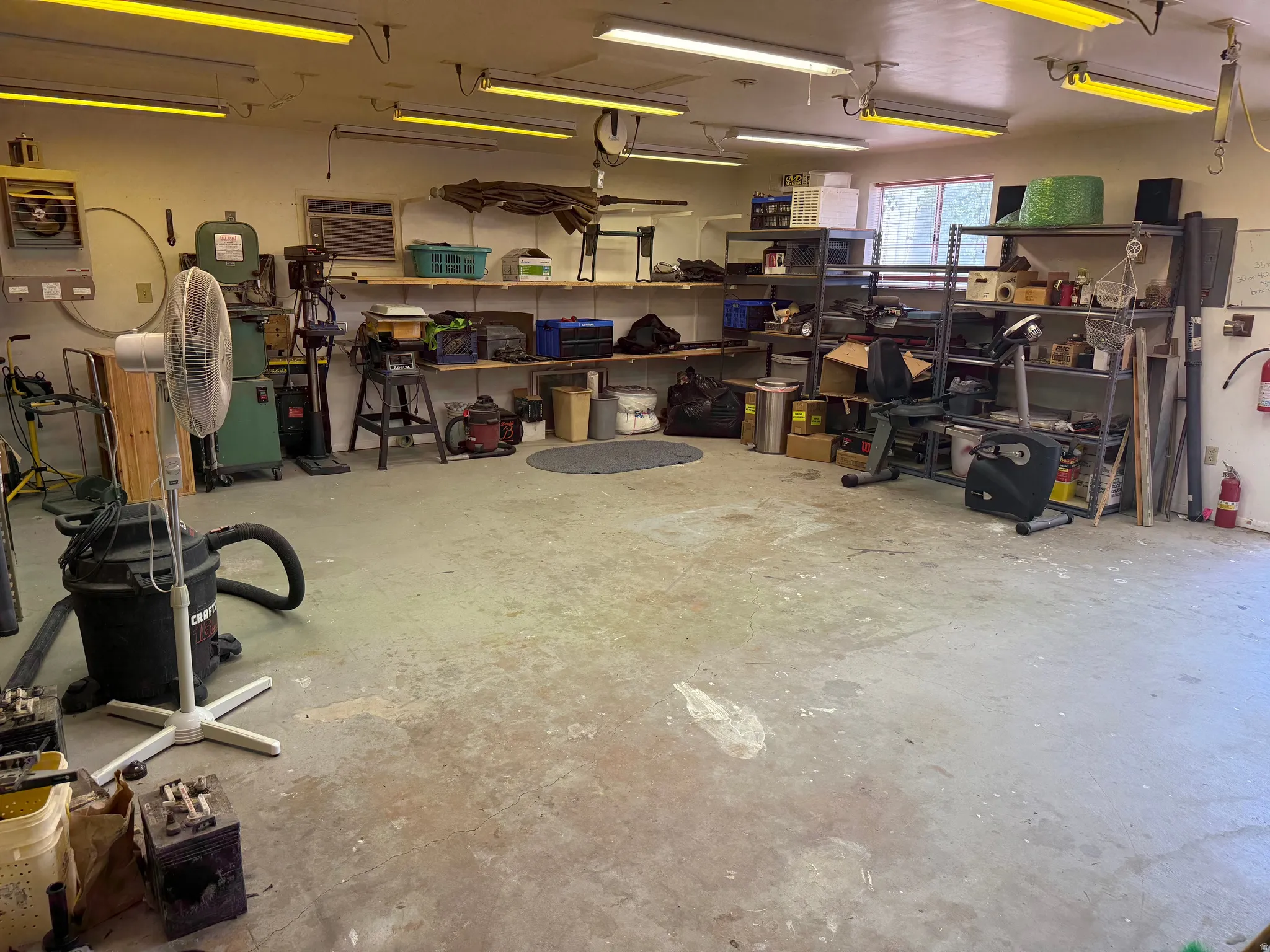 Spacious multi-purpose workshop featuring a concrete floor, extensive overhead fluorescent lighting, built-in shelving, heat and A/C, dust collection system and a window