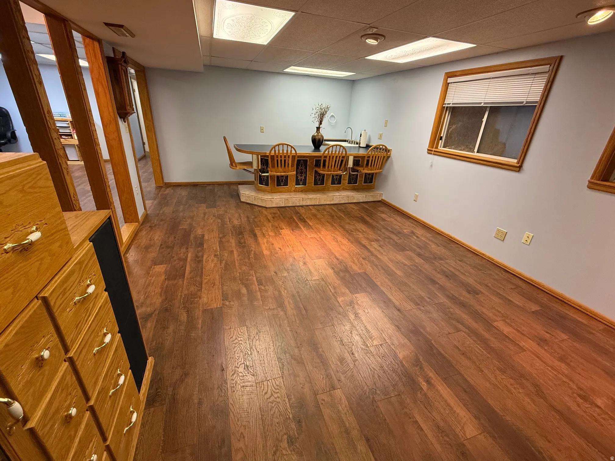 Spacious room featuring wood-finish flooring, a built-in wet bar with a tiled base, and light blue walls