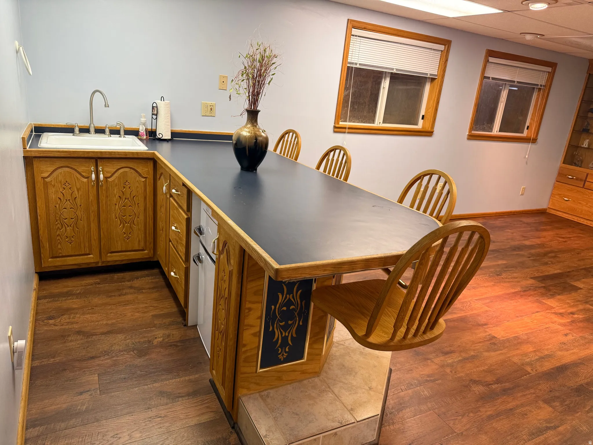 Wet bar featuring wood-finish flooring, light blue wall paint, and a built-in countertop with an integrated sink and   refrigerator, and 4 built in swivel seats