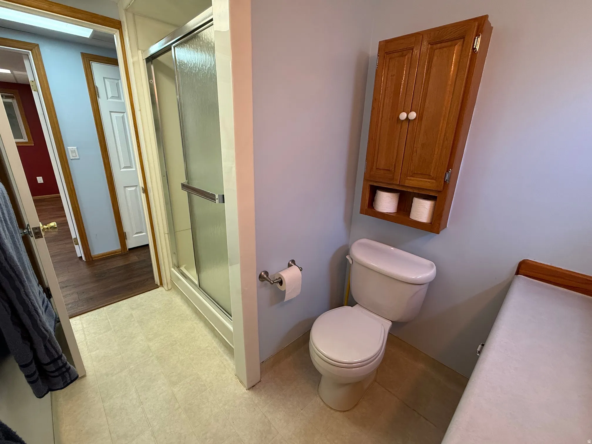 3/4 bathroom featuring a stand-alone shower with sliding glass doors, a wall-mounted wooden cabinet, and neutral-toned flooring
