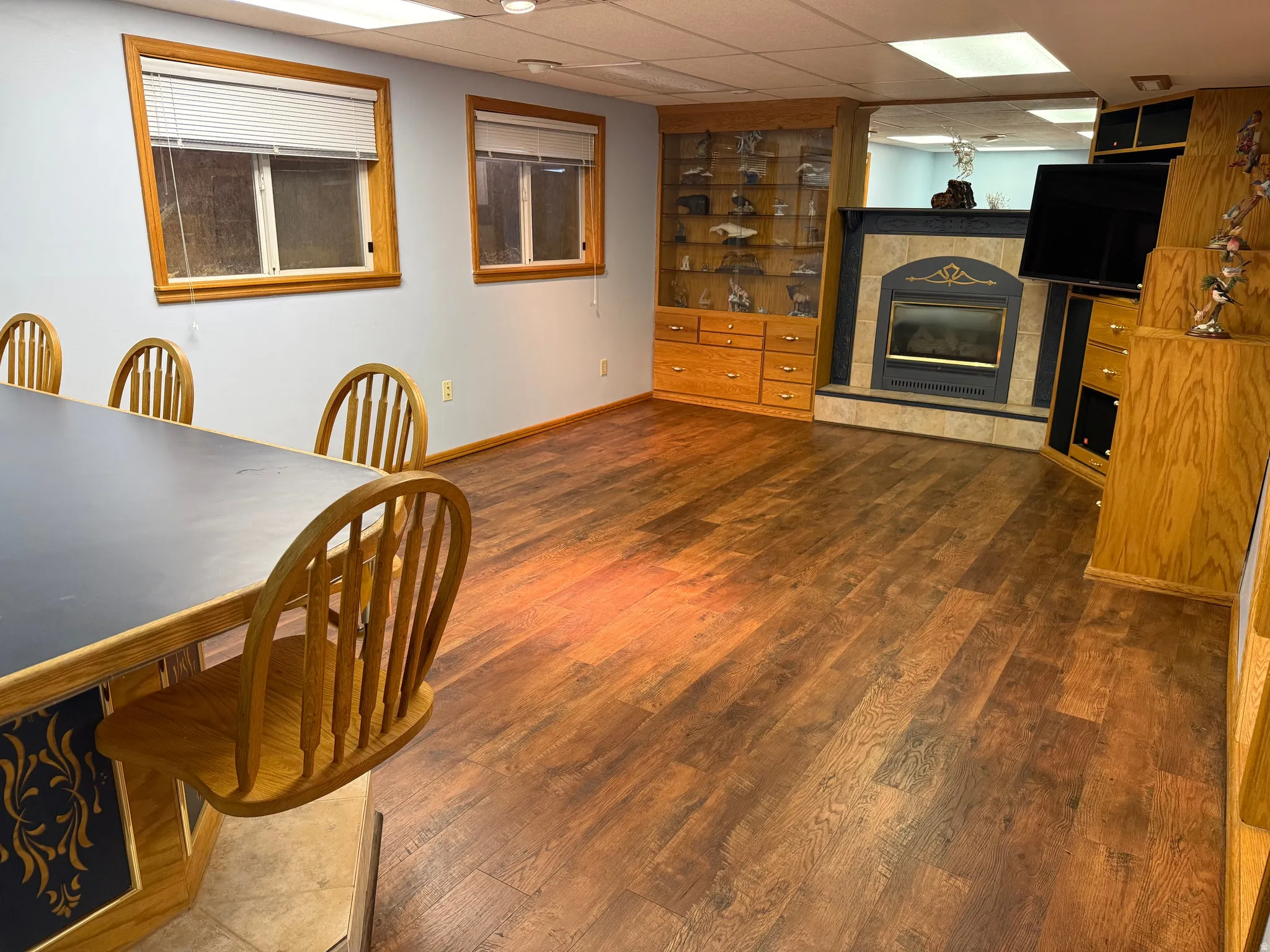 Spacious room featuring wood-finish flooring, light blue walls, and two windows with wood trim, fireplace.